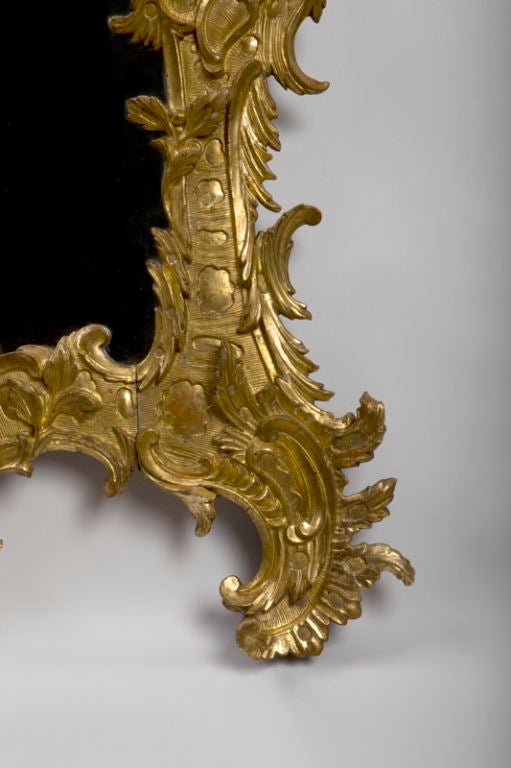 La placa rectangular del espejo' coronada por una cartela asimétrica de espejos rocaille' dentro de un extravagante marco tallado con volutas foliadas.