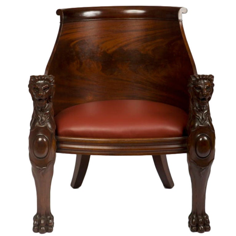 The mahogany barrel back with an outscrolled crestrail and a dark red leather bowed seat raised on back saber legs and <br />
lion's mask and cartouche-carved monopodia.