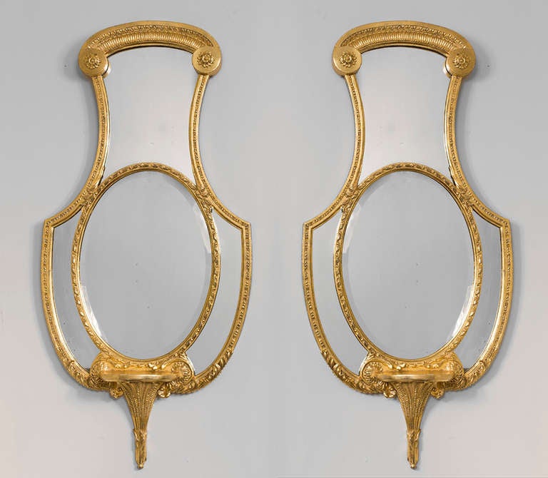 Each oval beveled mirror plate within a rope-twist frame, with an apron ending in a bracket, decorated overall with rosettes, foliage, leaf tips and fluting.
