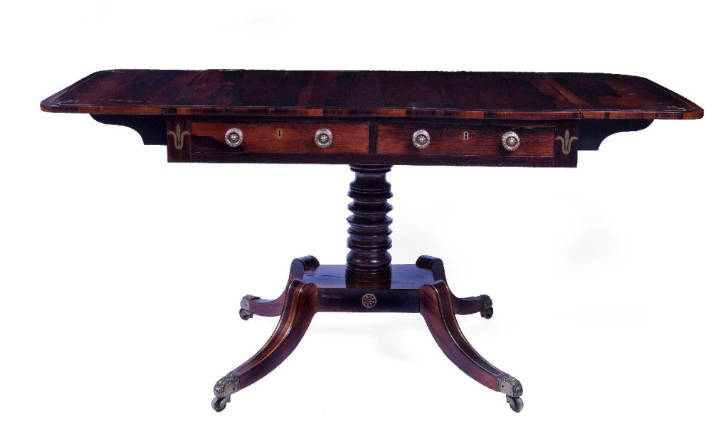 The rectangular top with rounded drop leaves, above two frieze drawers and two dummy drawers to the reverse, raised on a faux-rosewood grain painted ring-turned standard continuing to four hipped down-scrolling legs ending in leaf-cast casters.