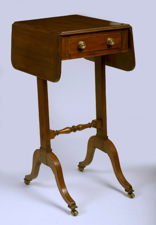 The rectangular crossbanded top with rounded drop-leaves and a single frieze drawer, raised on standards ending in splayed legs with casters, joined by a turned stretcher.