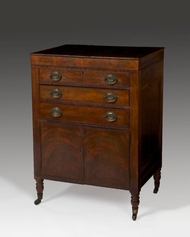 The hinged top enclosing a central well flanked by compartments, above one faux drawer and two long drawers and a pair of doors raised on turned feet ending in casters.