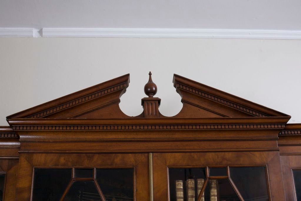 The dentil molded cornice with a triangular broken pediment above astragal glazed doors enclosing adjustable mahogany edged shelves‚ above four doors enclosing more shelves‚ on a plinth base.