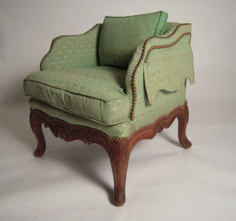 A  charming diminutive Louis XV style armchair, in carved fruitwood with green upholstery, the arms with scalloped flaps over side pockets.

Ideal as a decorative and functional small chair.

Provenance: John Cottrell, Stillington Hall,