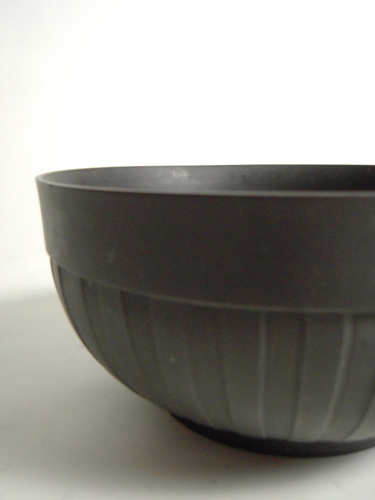 A 19th century neoclassical Wedgwood black basalt stoneware bowl with  a wide band over vertical, ribbed, engine-turned decoration, on a foot ring, with impressed 'Wedgwood'  mark on base.