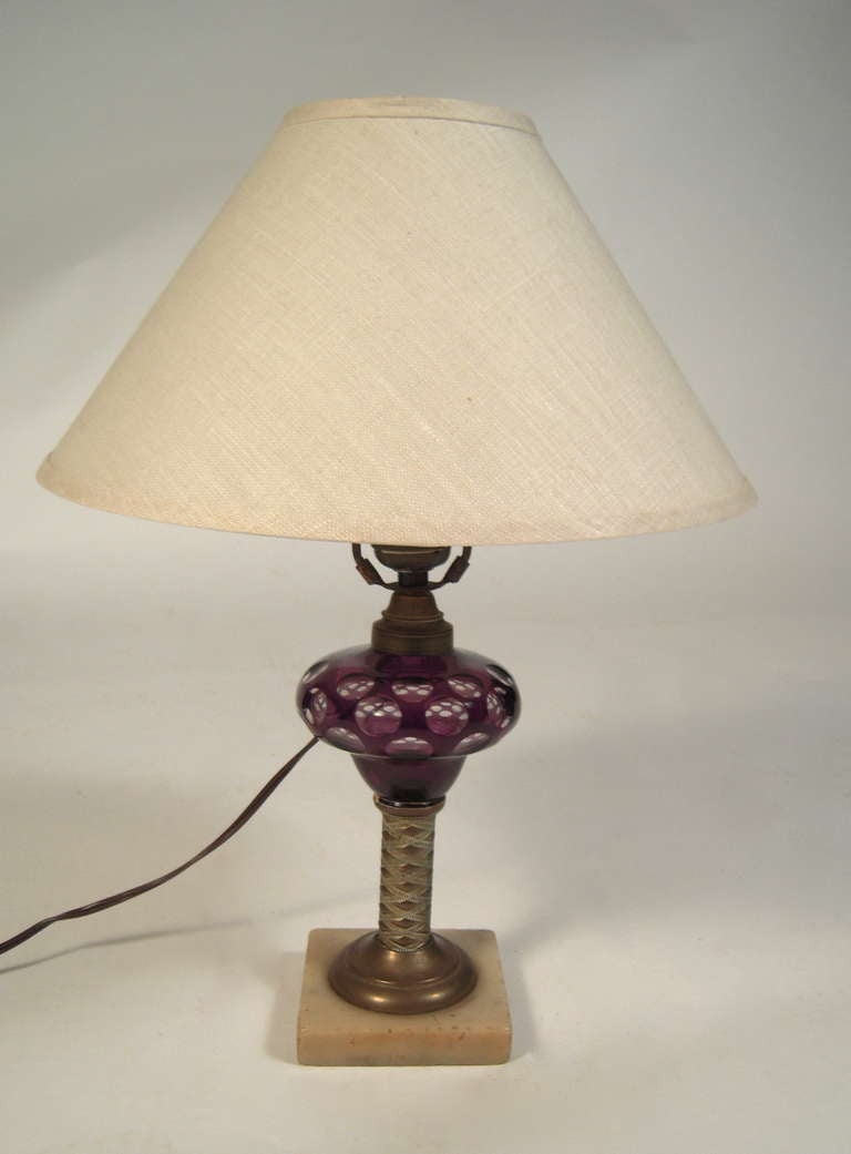A 19th Century amethyst cut to clear glass whale oil lamp on an embossed brass column mounted on a square marble plinth base. Electrified.