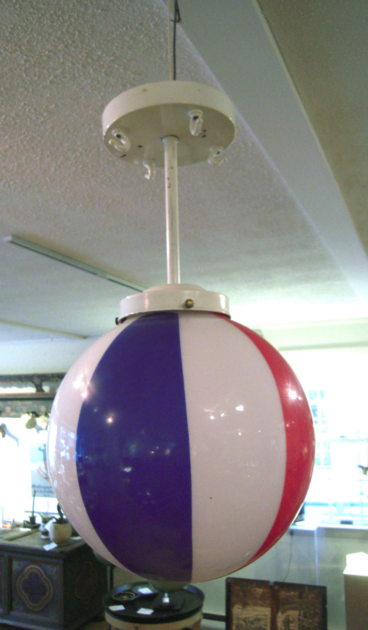 A graphic red, white and blue glass globe hanging light fixture, originally made for the American Basketball Association (ABA, 1967-1976), attached to a removable white-painted metal rod and ceiling canopy which has three hooks attached it