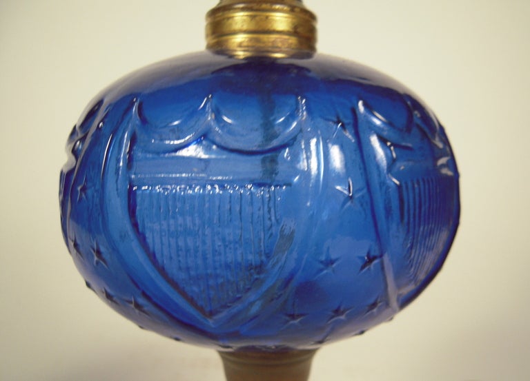 A pair of 19th century patriotic whale oil lamps, the cobalt blue fonts with raised American stars and striped shields over fluted and shaped milk glass bases. Newly re-wired, with new white paper shades and red glass finials.