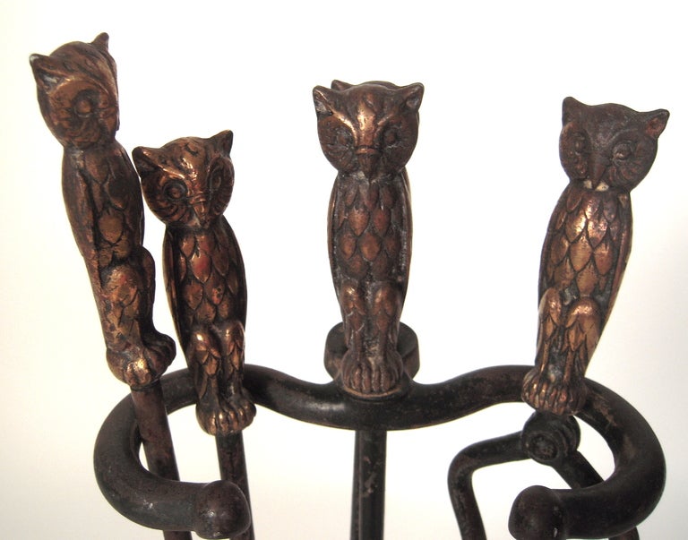 A charming and complete set of brass and iron owl-decorated fireplace tools comprising tongs, a poker, shovel and broom with holder, all in cast iron with brass owl modeled handles.