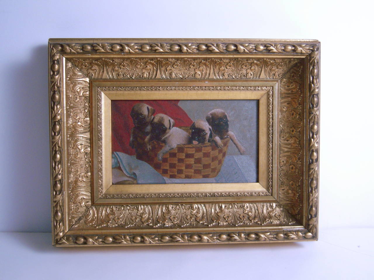 A charming, small painting depicting four pug puppies in a basket, circa 1870s, oil on artist's board, in a deep, gilded period frame. Unsigned. The back of the painting retains an original label from a 19th century New York City art supply shop.
 