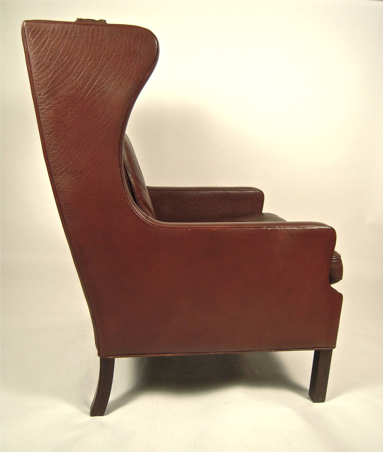 A  vintage Danish brown leather upholstered wingback chair in the manner of Borge Mogensen, the gently slanted back with serpentine side wings sloping down to form square section armrests, with one back cushion and one head rest and a seat cushion,