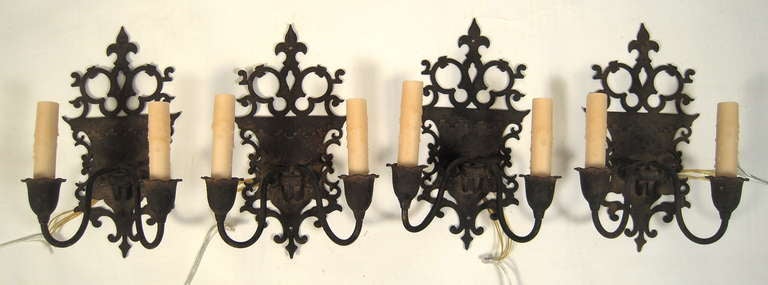 A set of 4 Renaissance Revival Italianate wrought iron sconces, the shield-shaped backs surrounded by open scrollwork and surmounted by fleur-de-lys. Newly re-wired with beeswax candle sleeves.