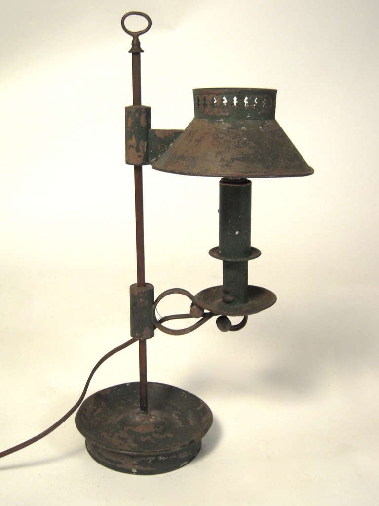 A wonderfully patinated French tôle lamp in original crusty green/black paint, the adjustable height shade with perforated gallery on a ring topped iron support with electrified candle, issuing from a circular base.

Provenance: Henry Davis 