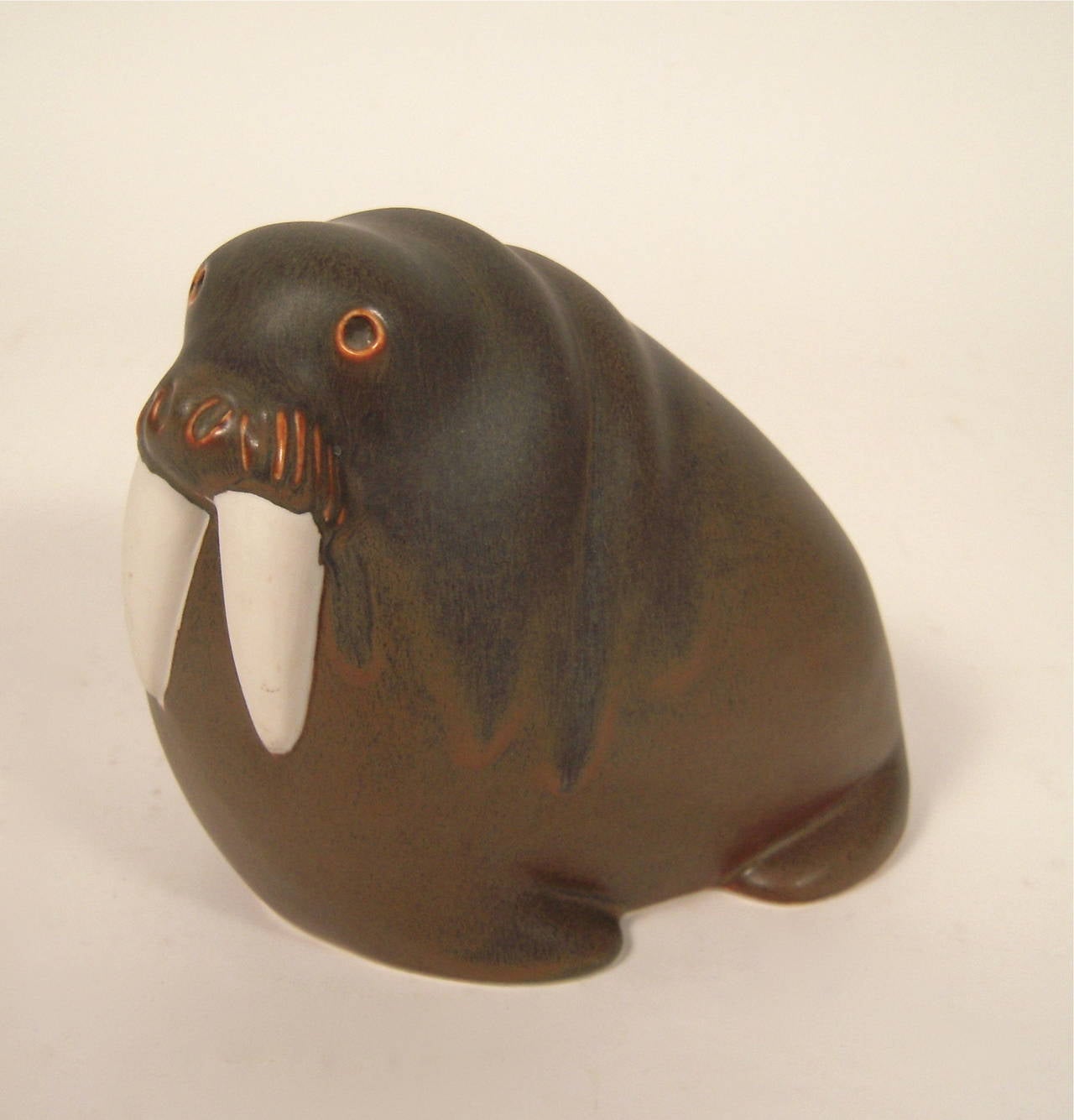 A vintage mid-century pottery sculpture of a walrus, designed by Taisto Kaasinen for Arabia Pottery, Finland, circa 1960,  glazed in matte brown and bluish tones with cream colored tusks, signed. 2 available.