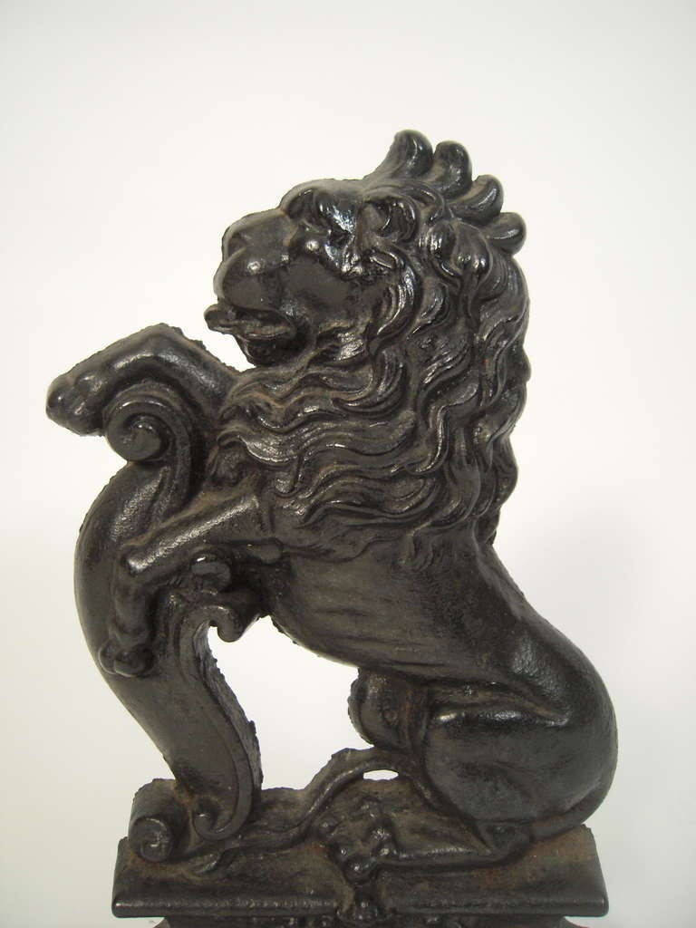 A generously proportioned , black painted cast iron door stop,  the seated lion with  its front paws resting on a scrolled element, its haunches supported on a shaped plinth with decorative, raised scrollwork on the front. 

This pose is used in
