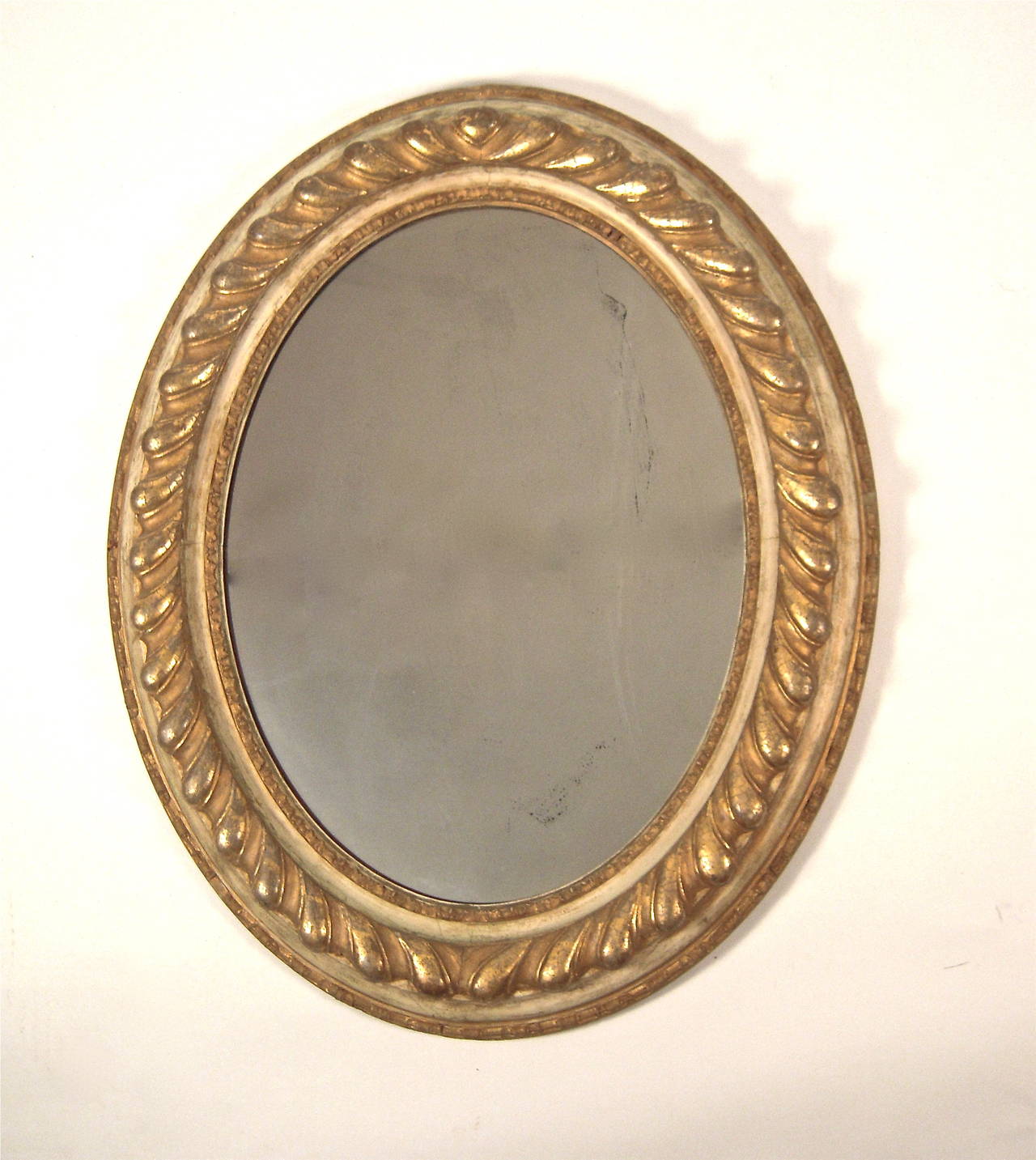 A 19th century neoclassical Italian oval giltwood mirror with gilded gadrooned border in high relief surrounded by bands of cream colored paint and gilded borders, with original mirror glass.