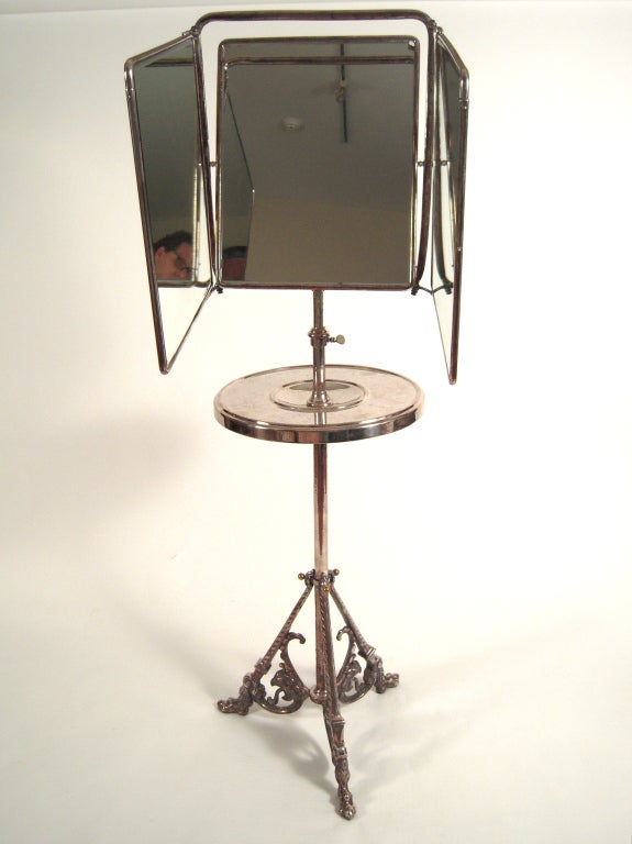 A sculptural and useful, adjustable height luxurious silver plated shaving stand with 3-part folding mirror of beveled glass, the reverse of the central mirror in faux snakeskin, the other 2 panels backed with iris decorated embossed paper