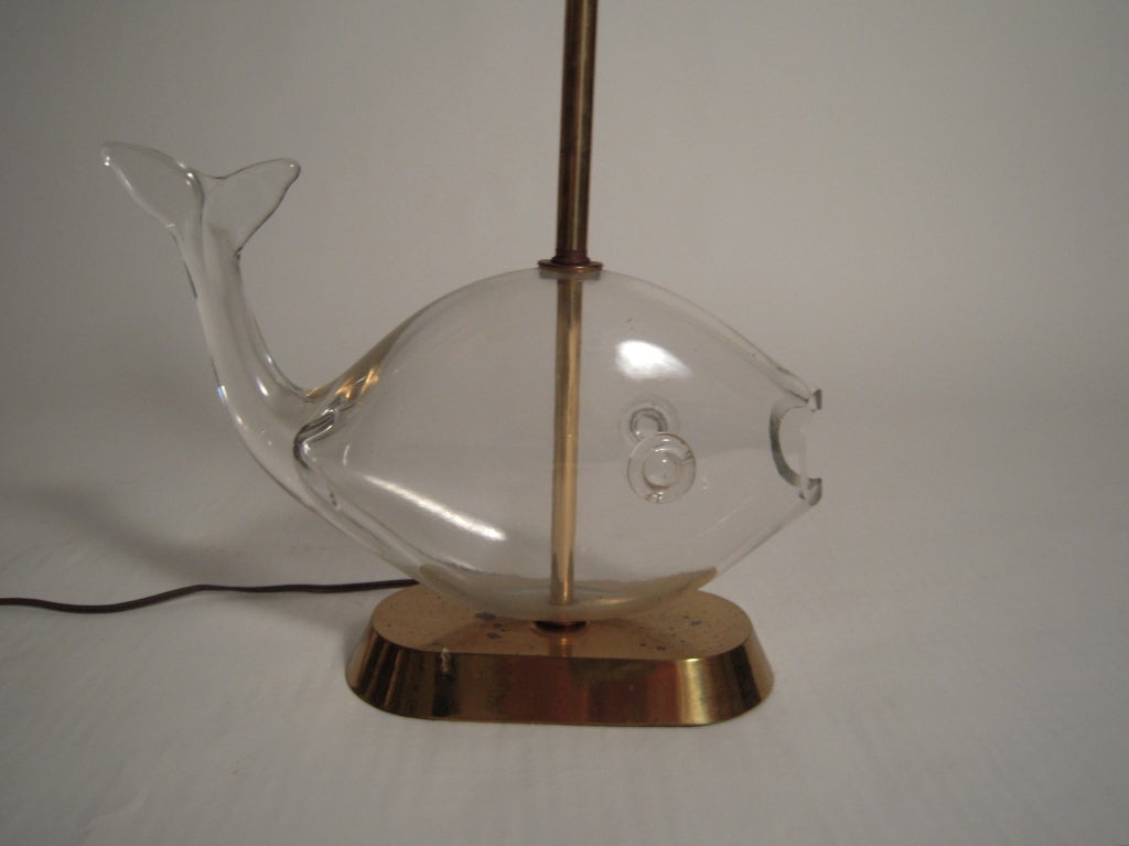 A stylish Italian, clear blown glass whale fish-form lamp, on an oval antiqued brass base, likely by Empoli. With new white linen oval shade and clear glass ball finial.
