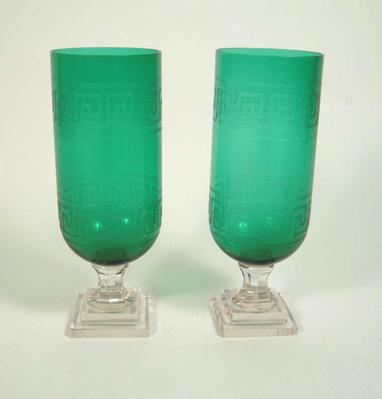 A pair of Regency style green and clear crystal hurricane shades,  the green portion etched with two bands of Greek key decoration, one at the top, one at the bottom, on a clear crystal stepped square plinth.

15 5/8
