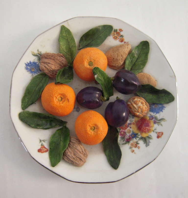 A French trompe l'oeil ceramic food plate by Christine Viennet, the c. 1910 porcelain plate decorated with transfer printed flowers in various colors, to which later, realistically modeled ceramic clementines, plums. walnut shells and leaves have