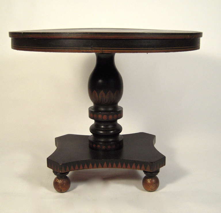 A 19th century American paint decorated, ebonized tilt-top center or occasional table, with strong graphic lines, the circular top with painted flowers in various colors on a black ground, over a frieze with painted red and yellow stripes, the
