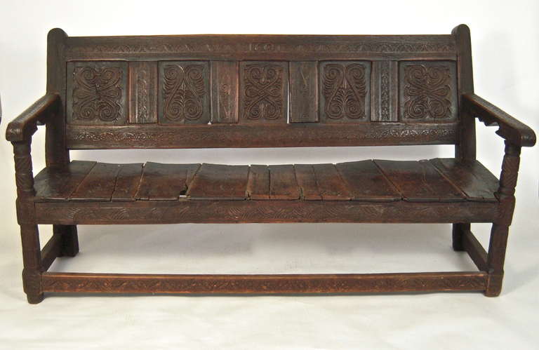 A boldly carved and well proportioned carved English Jacobean style settle, or bench, the top of the back with the year '1601' carved into the top rail, over inset panels carved with graphic scrolling and foliate decoration, flanked by two arms with