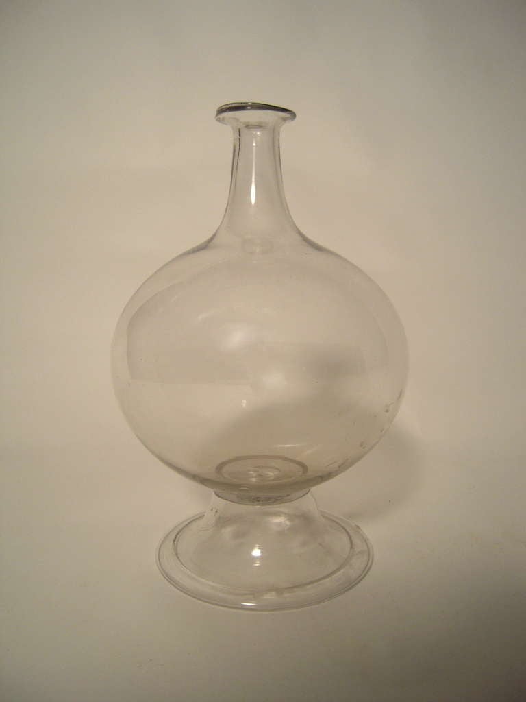 An 18th century colorless blown glass lace maker's lamp, of bulbous form, the tapered neck with everted rim, on a spreading pedestal base with folded rim. Designed to magnify candle light for the intricate work of lace making, also ideal as a vase.