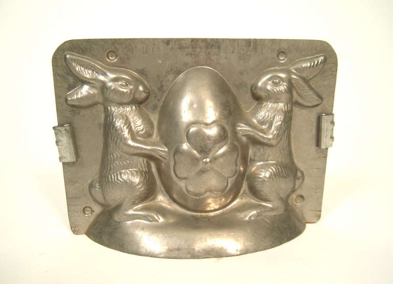 A vintage cast aluminum 2-part chocolate mold, in the form of 2 standing bunnies flaming a large flower-decorated Easter egg.