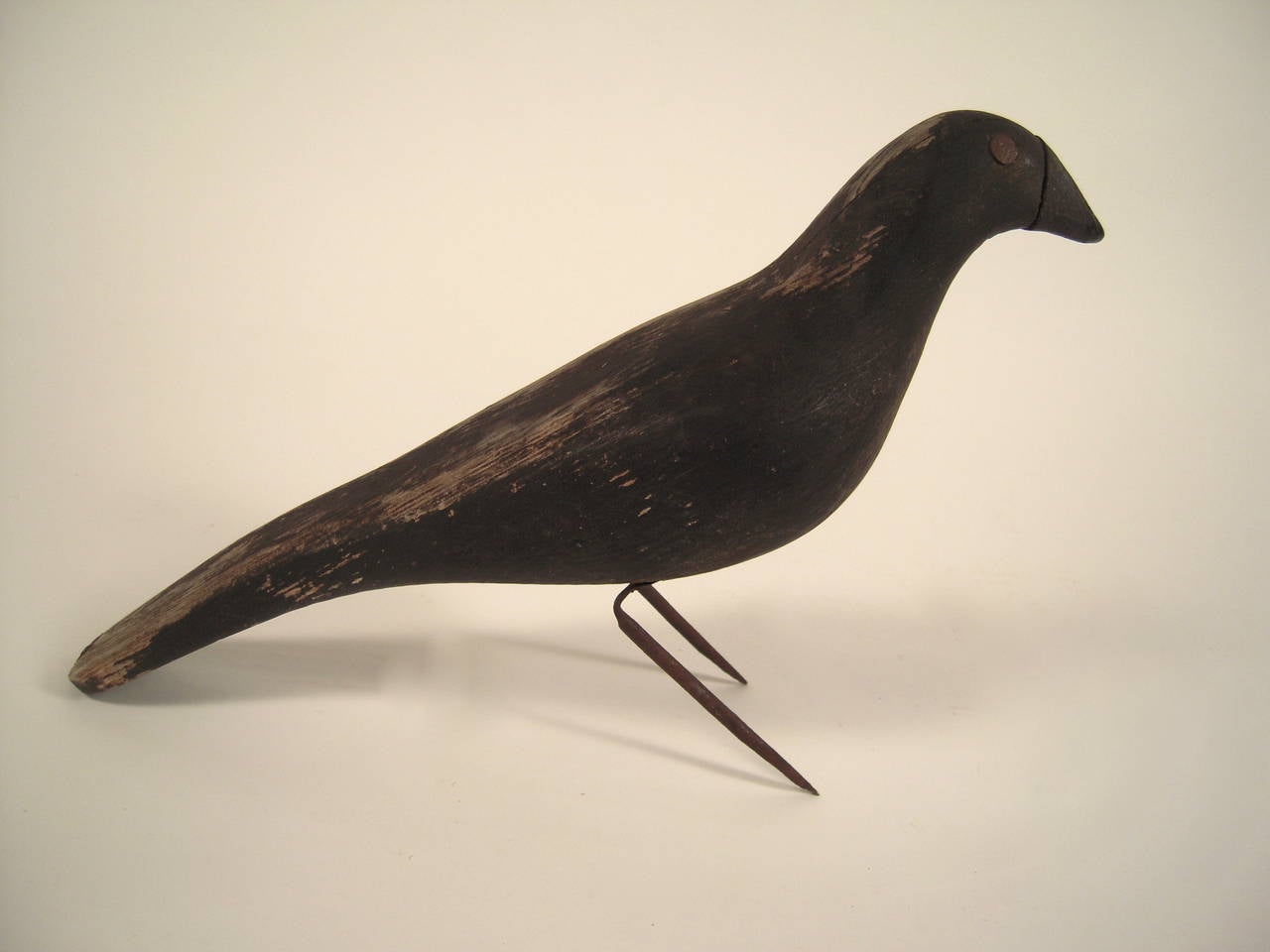 A folk art wood carved and black painted sculpture of a crow, with iron nail eyes and legs and with impressed 