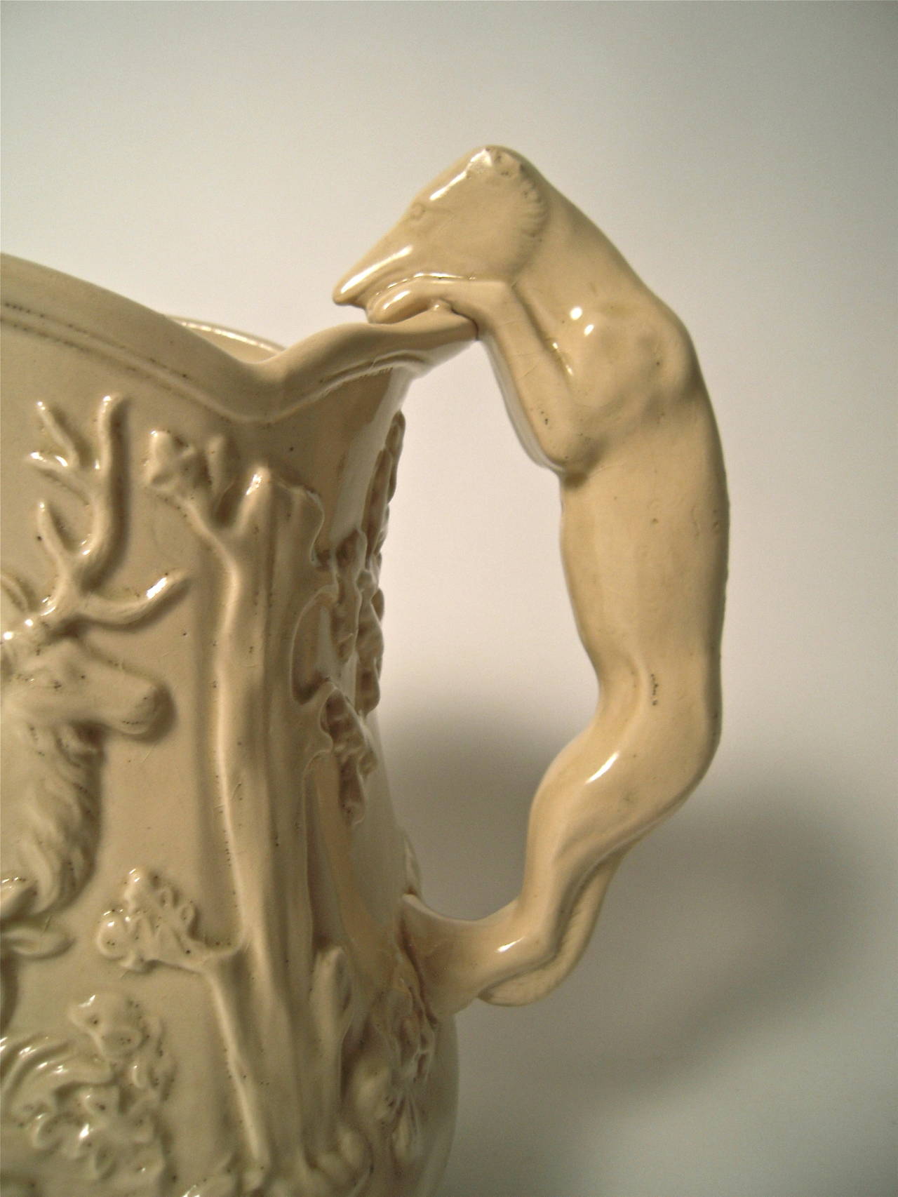 A large 19th century American yellow ware pottery hound-handled pitcher, made in the East Liverpool, Ohio potteries, with scalloped rim, the body decorated in relief with a stag and seated doe in a landscape, with a whimsical hound dog handle,