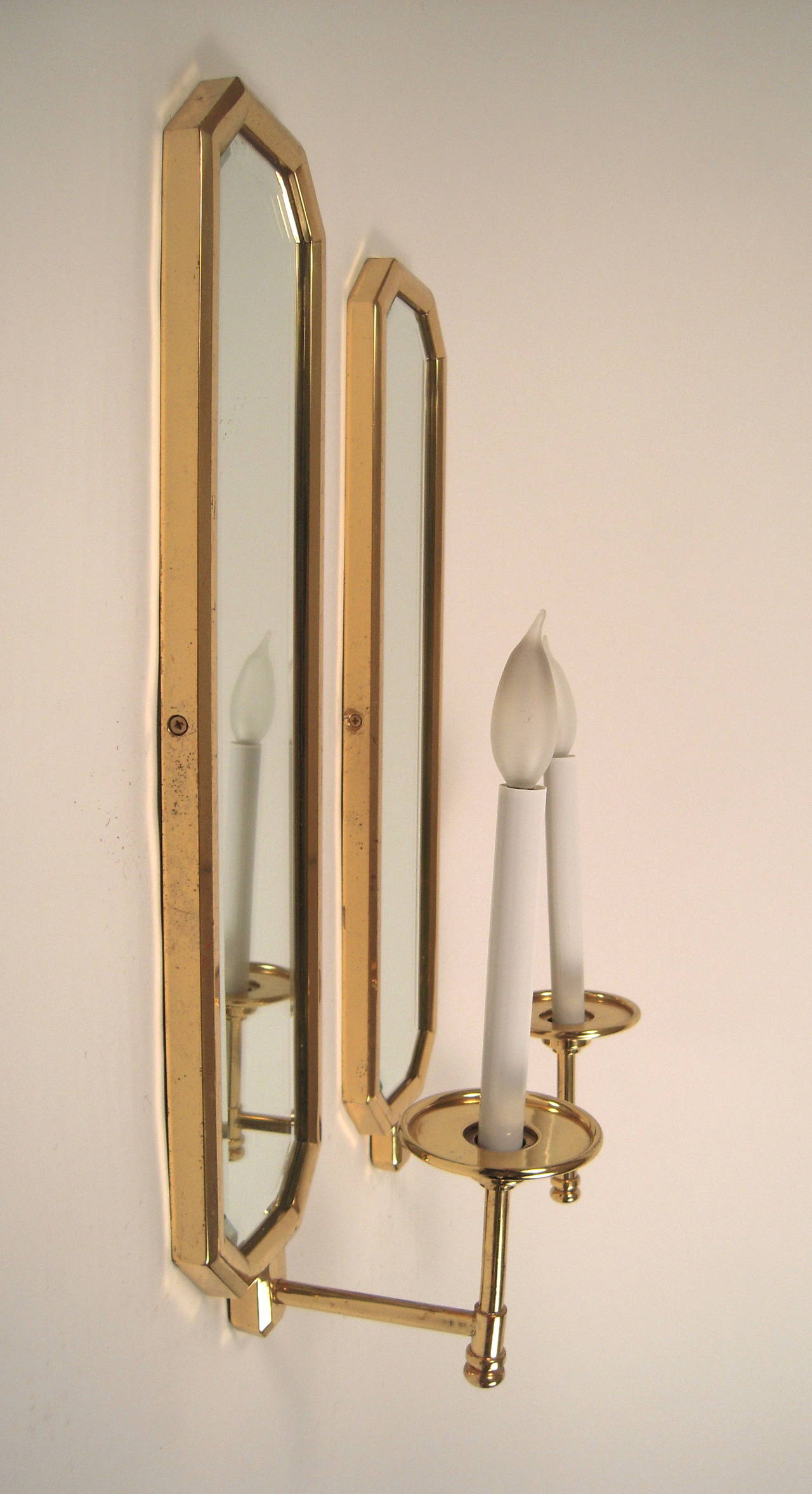 A pair of high quality brass and mirrored wall sconces by Chapman, circa 1970s, of elongated octagonal form, with well-made bevelled brass frames enclosing mirrored backplates, each with a single candle with cylindrical supports and wide bobeches,