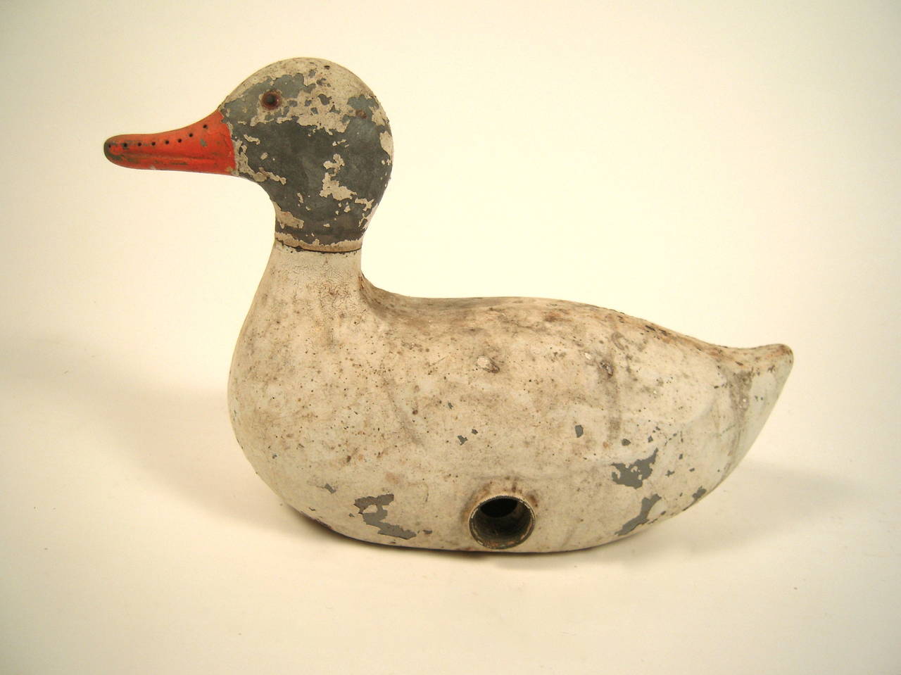 A whimsical cast metal duck sprinkler in old white paint with a turning grey painted head orange beak and one glass eye. The head, which is perforated for water to come out, is designed to rotate when functioning as a sprinkler. Whimsical.