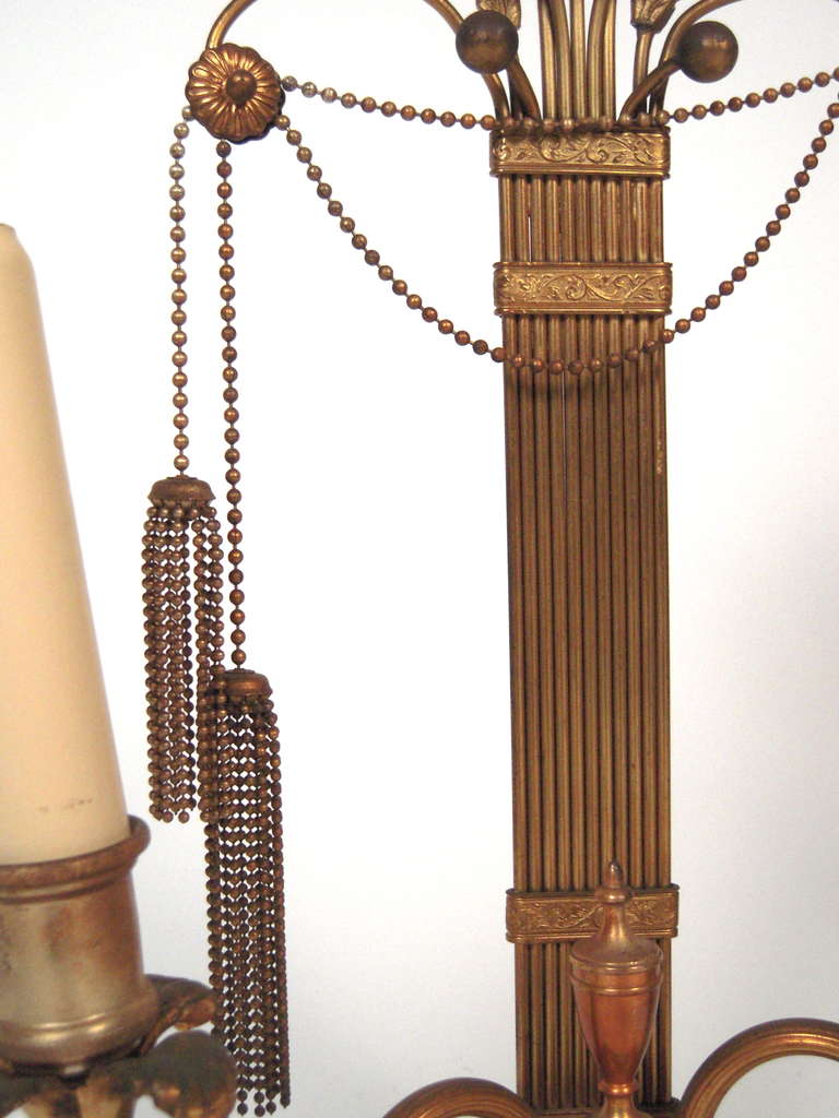 A pair of unusual and stylish Art Deco period neoclassical style (Hollywood Regency) candelabra lamps (currently electrified, but may be converted to candles), each surmounted by a fan of wheat over a fluted column draped with a swag of beaded chain