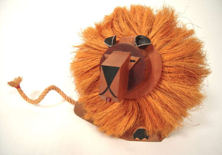 A mid-century modern lion pull toy, Japanese, circa 1950s-60s, in carved wood with leather ears and a coconut fiber mane and tale.