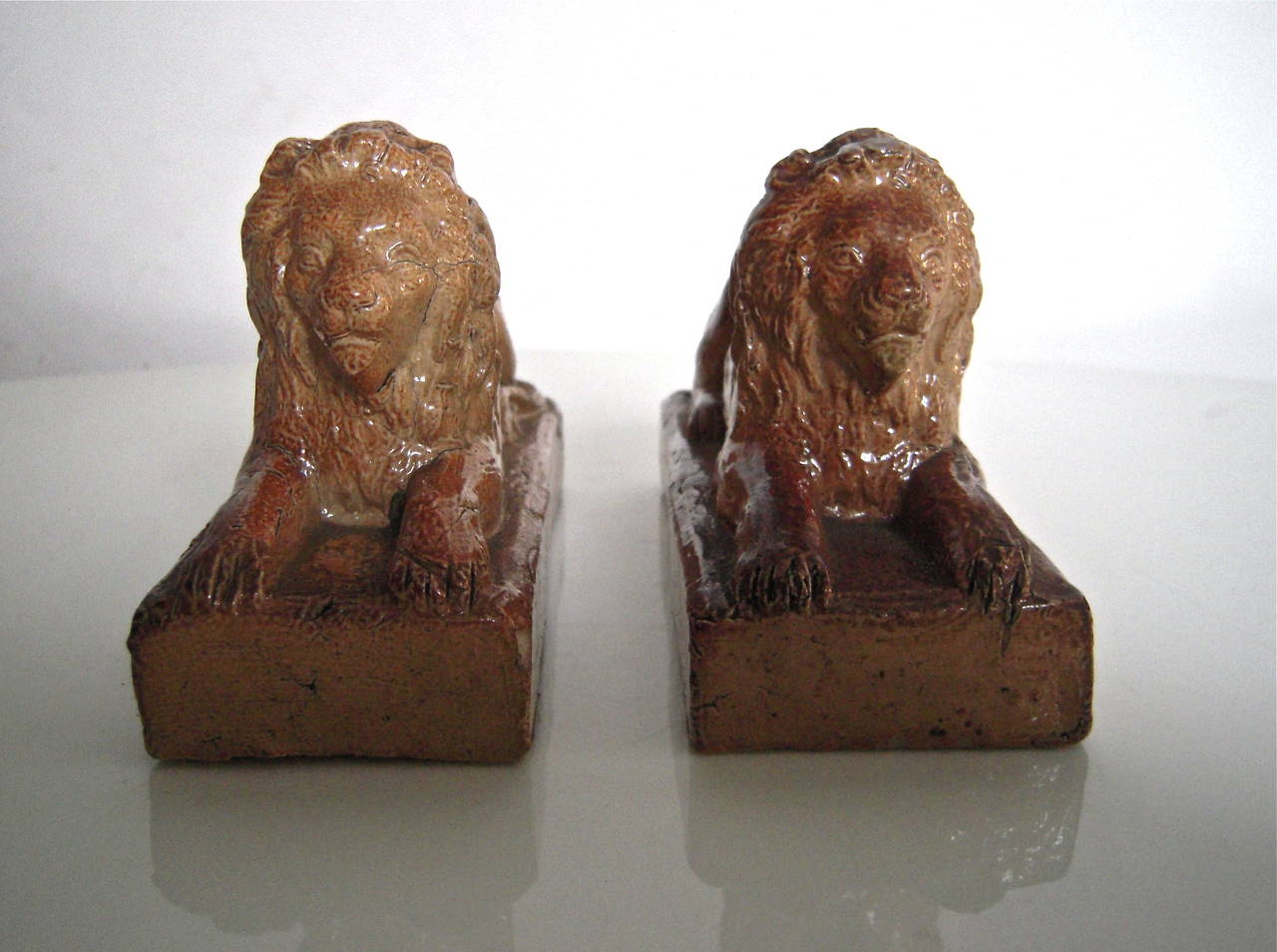 A pair of small 19th century English stoneware recumbent lions, on rectangular plinths, in glazed earthenware. Beautiful on a fireplace mantel or table.