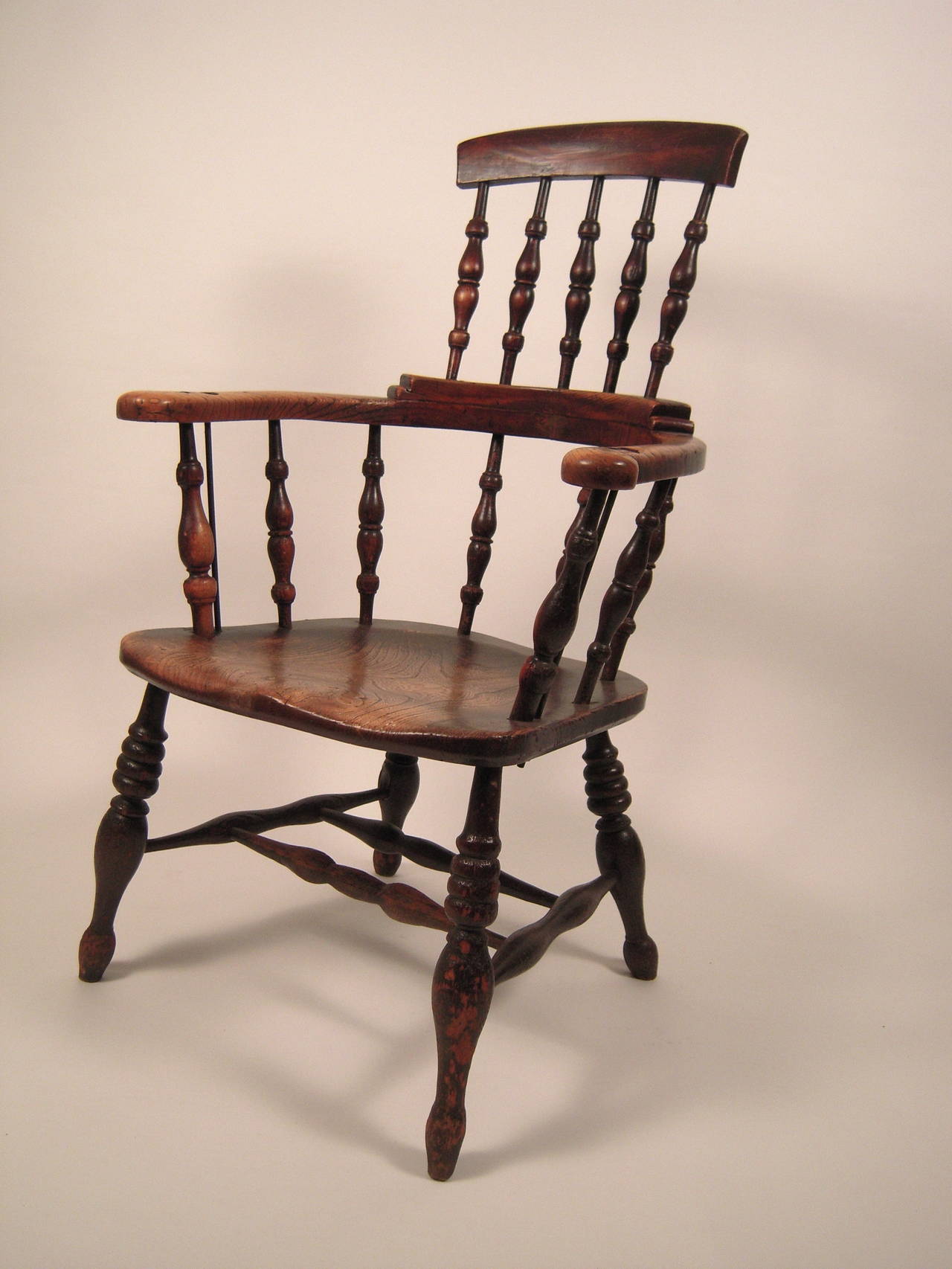 An English Country tavern chair in elm, circa 1830-1840, with wonderful color and patina, with spindle back, curved arms, a shaped, solid elm plank seat supported by boldly turned legs joined by cross stretchers.
Old, but later, metal bolt and rods