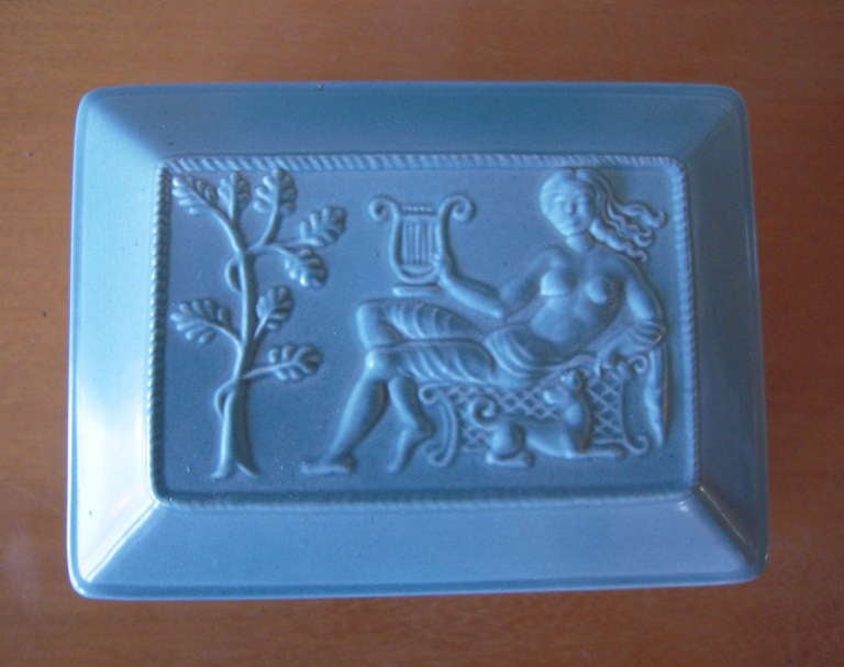 A 'ROYAL JADE' TURQUOISE GLAZED COVERED STAFFORDSHIRE POTTERY BOX BY WEDGWOOD, WITH LOW RELIEF SCULPTED TOPS  DEPICTING STYLIZED VIRGO ZODIAC SIGN BY ERLING (ERIC) OLSEN, English, circa 1930s.

Dimensions:
H: 1 1/2