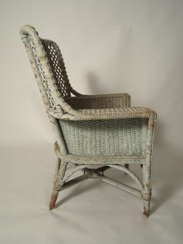 A celadon green painted wicker arm chair, generously proportioned, with a newly made seat cushion, down filled and upholstered in vintage Brunschwig and Fils 'Bird and Thistle' pattern fabric, coral, with yellow, green and blue highlights.