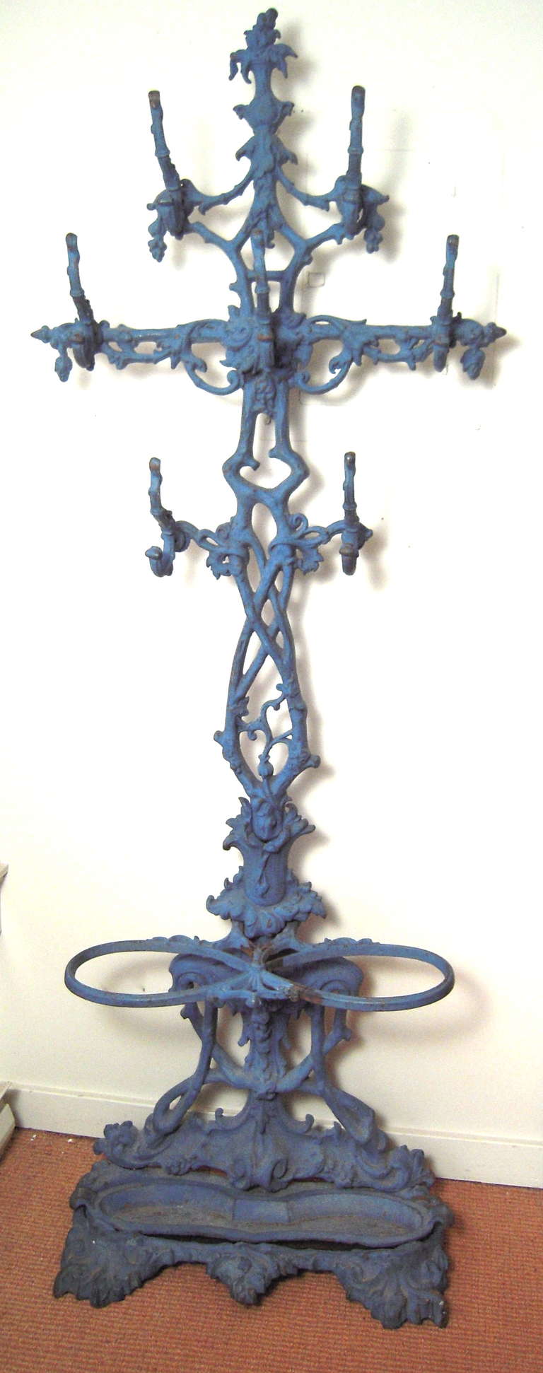 19th century blue painted cast iron hall tree with whimsical intertwined 'branch' support and hat and coat hooks, the base with loops to hold umbrellas and a drip pan.

In 2 sections which attach easily with screws.

