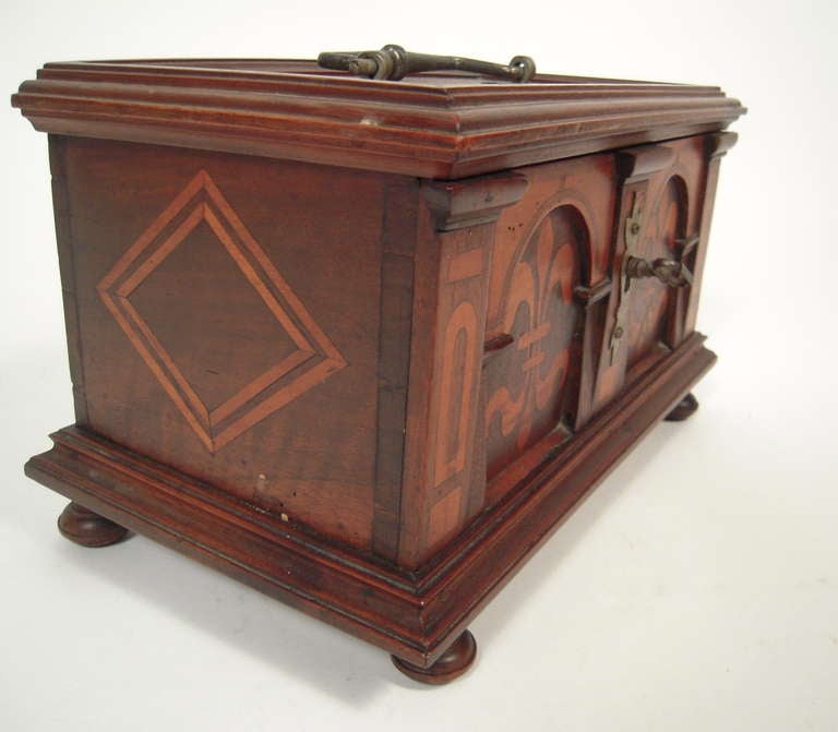 A Renaissance Revival Swiss marquetry wood  box with inlaid fleur de lis decoration within an arcaded architectural design, centered by a pewter escutcheon with key, the top and sides decorated with inlaid geometric decoration and with a pewter bail