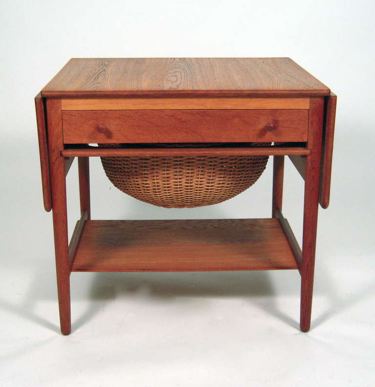 A Hans Wegner designed sewing table, made by cabinet maker Andreas Tuck, in stained oak, the square top flanked by two extendable leaves, over a drawer with compartments for storage of spools of thread and other sewing supplies, over a sliding tray