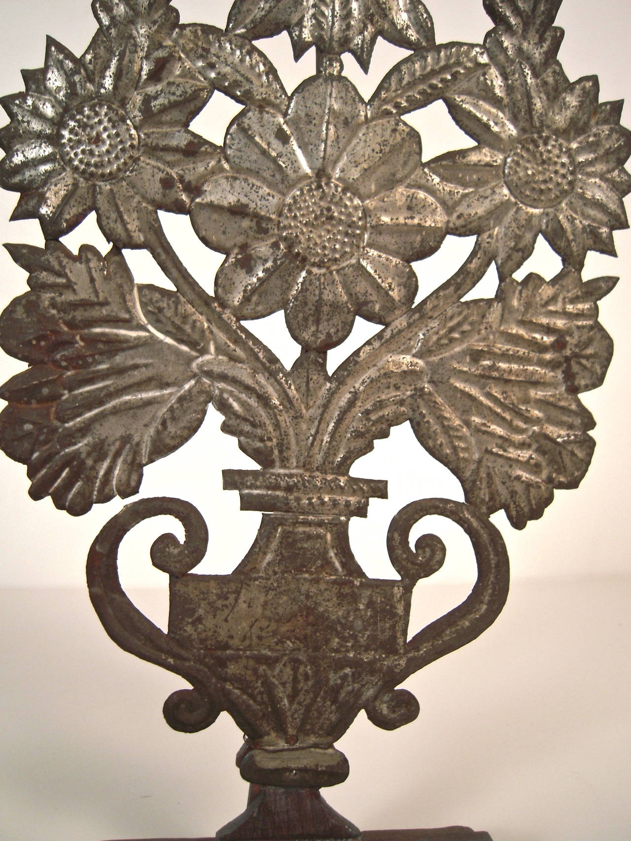 A charming and decorative pressed repousseé tin decoration in the form of a neoclassical urn containing an exuberant flower arrangement, mounted on a stained wooden stepped plinth. Possibly Mexican?

Measure: H: 17 1/4
