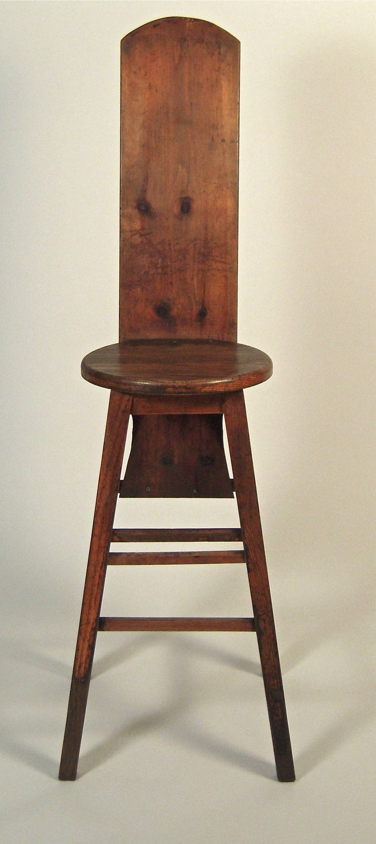 A sculptural and completely useable, tall back high stool, in walnut stained oak and pine, designed and made as a child's punishment stool, the round seat, square section legs and foot rests in oak, the tall, angled back with arched top in pine. The