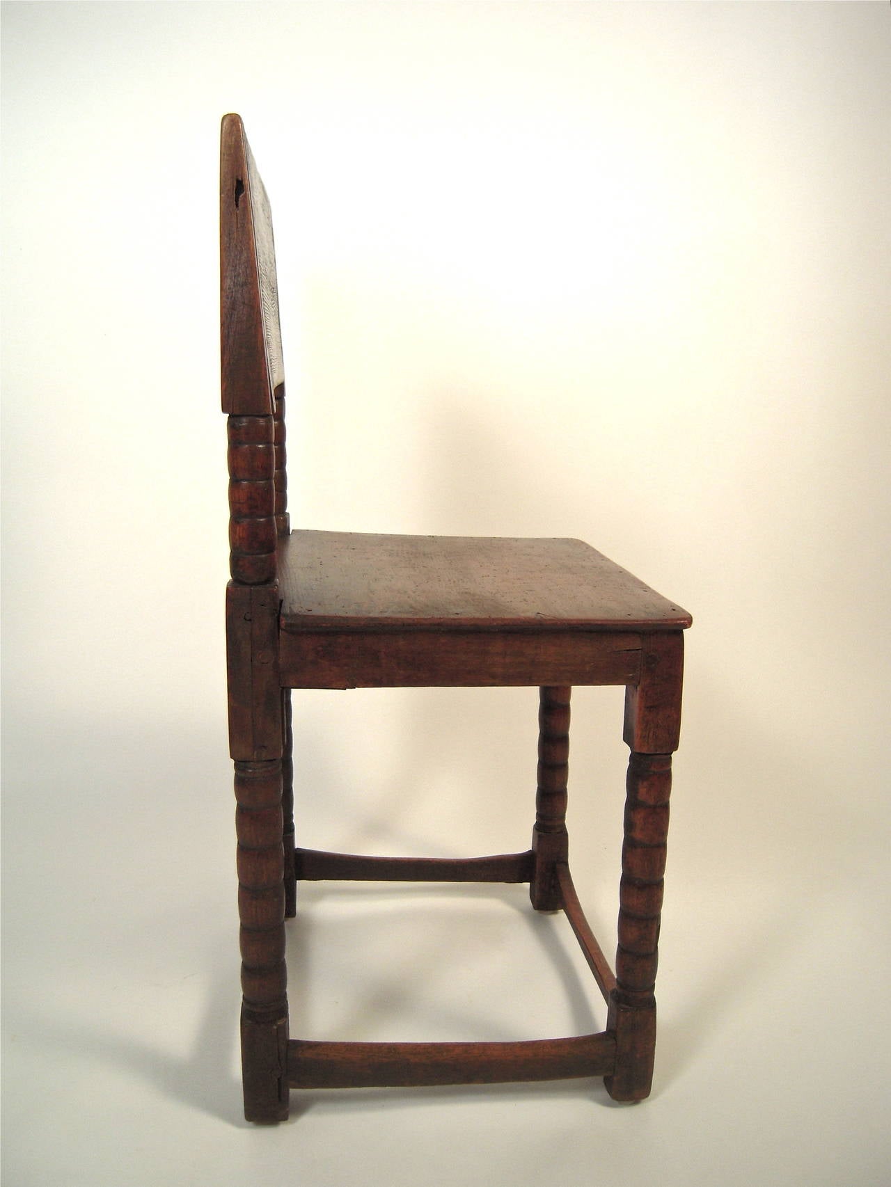 A 17th century English  Cromwellian chair with plank back and seat in walnut stained pine, the rectangular solid back over sausage turned supports over conforming seat raised on four sausage turned legs, joined by wonderfully well-worn cross