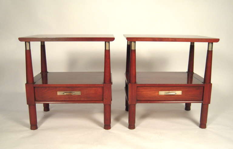 A pair of end tables in mahogany stained cherry, the rectangular tops with curved edges supported by four columnar supports with metal collars at the top over a shelf and single drawer with nautical cleat pull, raised on four cylindrical feet.