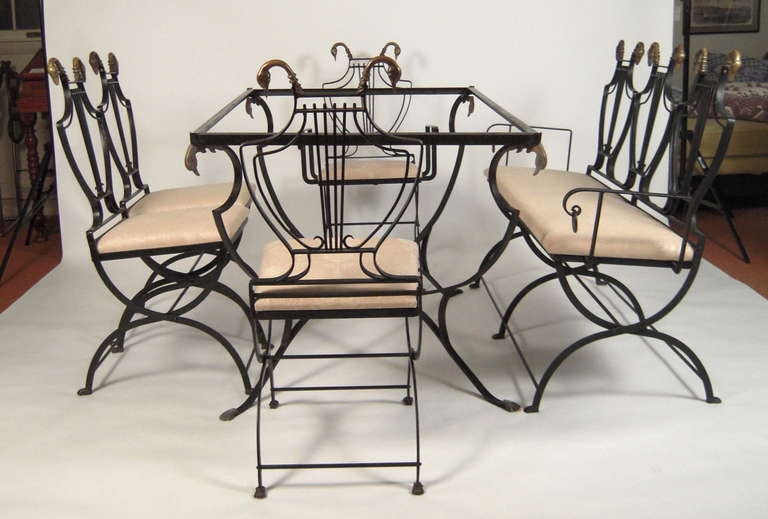 A neoclassical style/Hollywood Regency dining table and chairs (3 side chairs, 1 arm chair)  and settee for 6, the black painted wrought iron  iron lyre-back folding chairs with bronze swan's head decorations, over upholstered seats, raised on