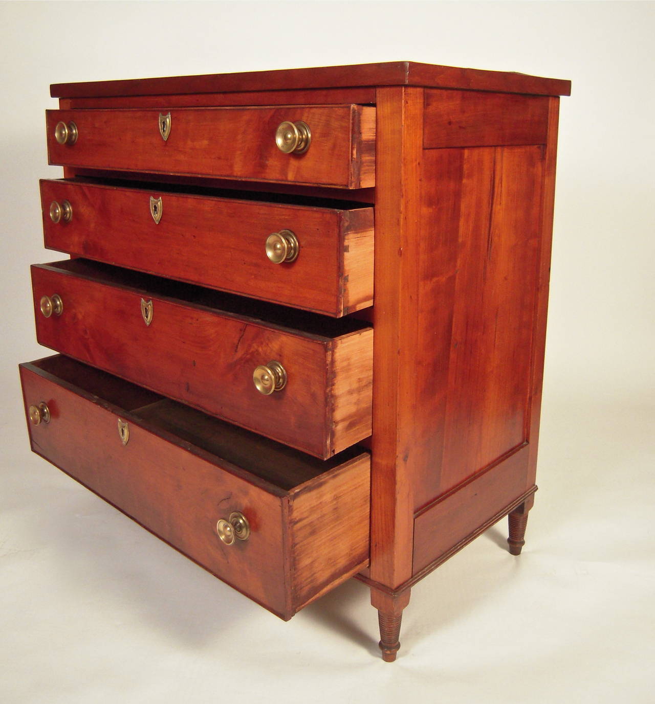 A Biedermeier classically proportioned chest of drawers in cherry, circa 1830s, the rectangular case with 4 cockbeaded, graduated drawers, each with 2 brass drawer pulls and centered by shield shaped brass escutcheons, raised on 4 tapered spirally