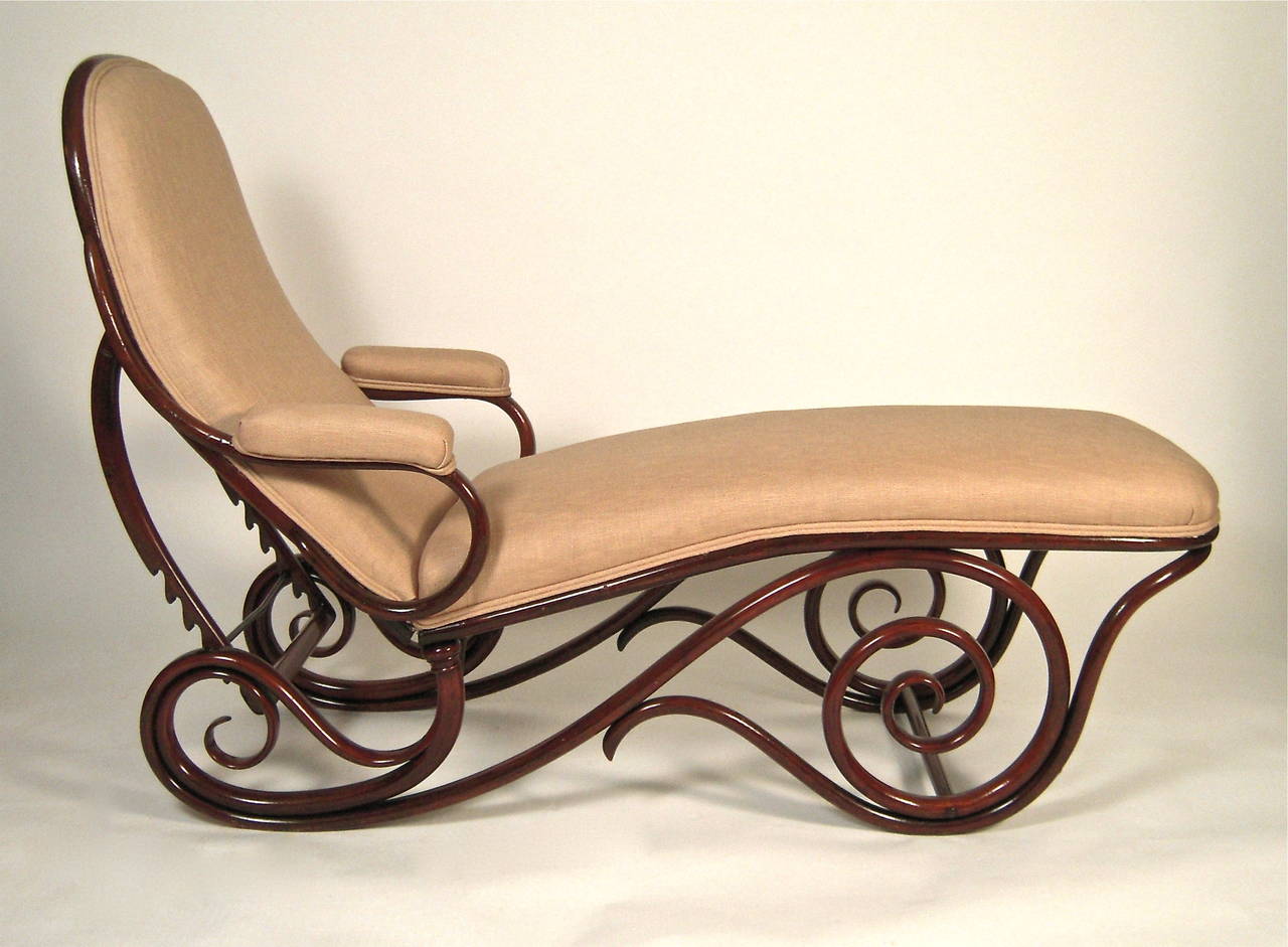 A Thonet bentwood chaise longue in mahogany stained bentwood, the new linen upholstered seat, arms and adjustable height back over an exuberantly scrolled base. The ratcheted back support allows for a wide range of angles for lounging. First