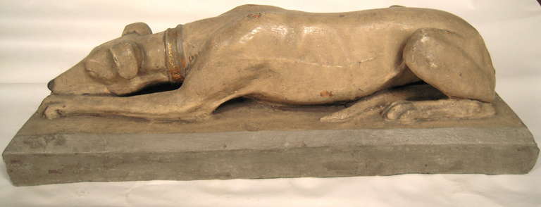 A pair of well modeled 19th century cast, painted and partially gilded terra cotta recumbent greyhound sculptures, naturalistically modelled, in old buff stone colored paint. with later gilded collars,  on grey, integral rectangular plinths. These