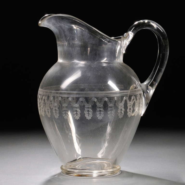 A large 19th century clear blown glass pitcher with engraved decoration,circa 1860-80, of  baluster-form with applied ear handle, with medial engraved bands of interlaced ovals, and undulating lines and tassels, with polished pontil. 

Height 12